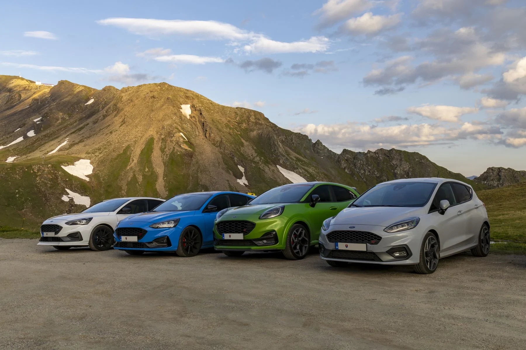 Cuatro autos estacionados juntos frente a una cadena de montañas